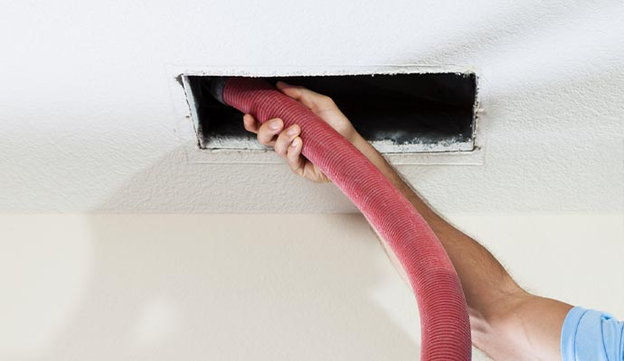 A person cleaning an air duct in the ceiling
